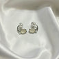 A pair of silver-toned C-shaped hoop earrings with oval cream-colored stones and small pearl-like beads, displayed on draped white satin fabric.