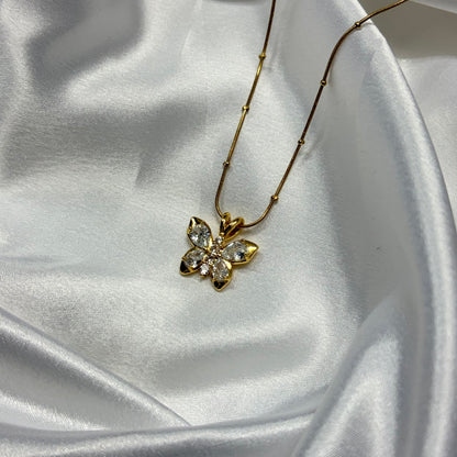 A gold flower pendant necklace with clear crystals, resting on draped white satin fabric.