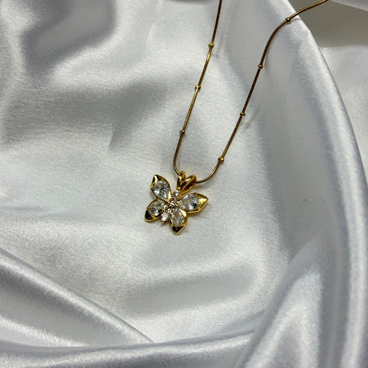 A gold flower pendant necklace with clear crystals, resting on draped white satin fabric.