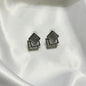 A pair of geometric stud earrings with layered square and rectangular silver-tone frames, one featuring a smooth dark gray inset and the other accented with small clear stones, displayed on a white satin fabric background.