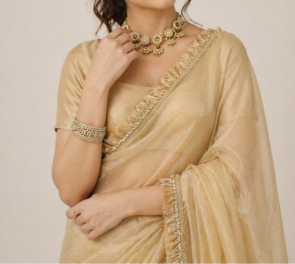 Woman wearing a beige saree with gold embroidery against a plain background
