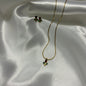 A gold necklace and matching stud earrings with small red rose-shaped stones and green leaf accents, displayed on draped white satin fabric.