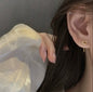 Close-up of an ear wearing a gold heart-shaped earring with a blurred background.