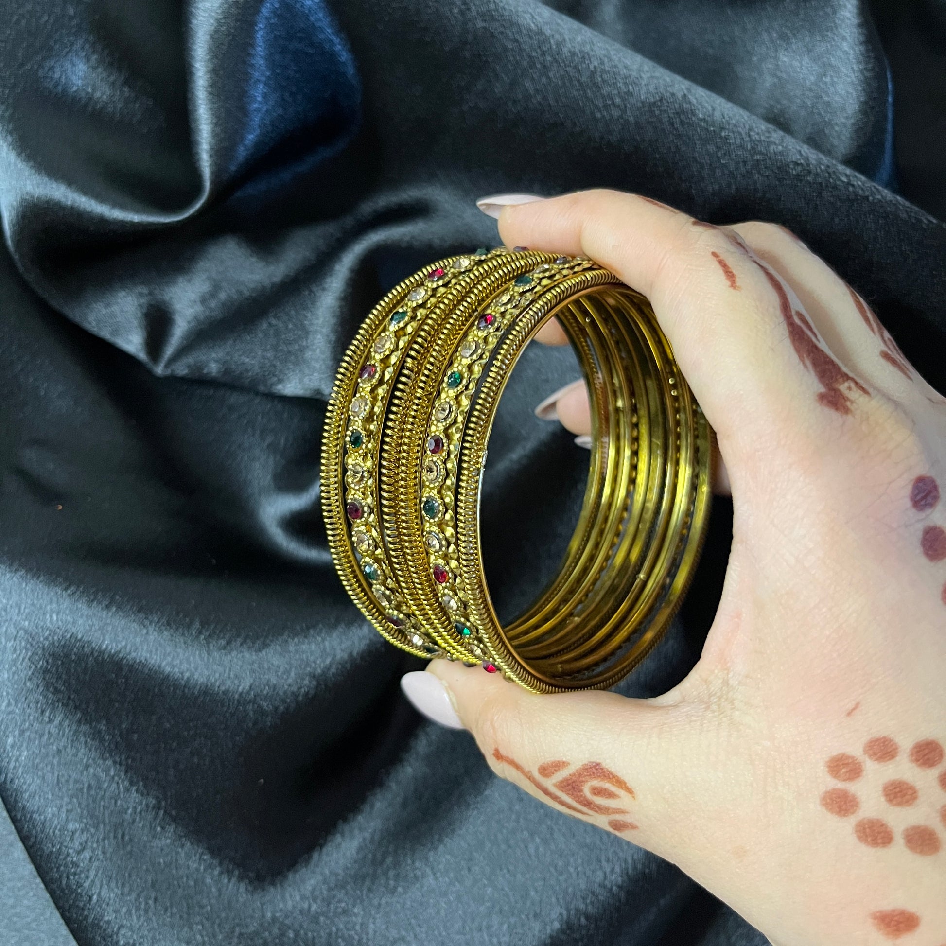 Hand holding gold bangles with intricate designs against a dark fabric background